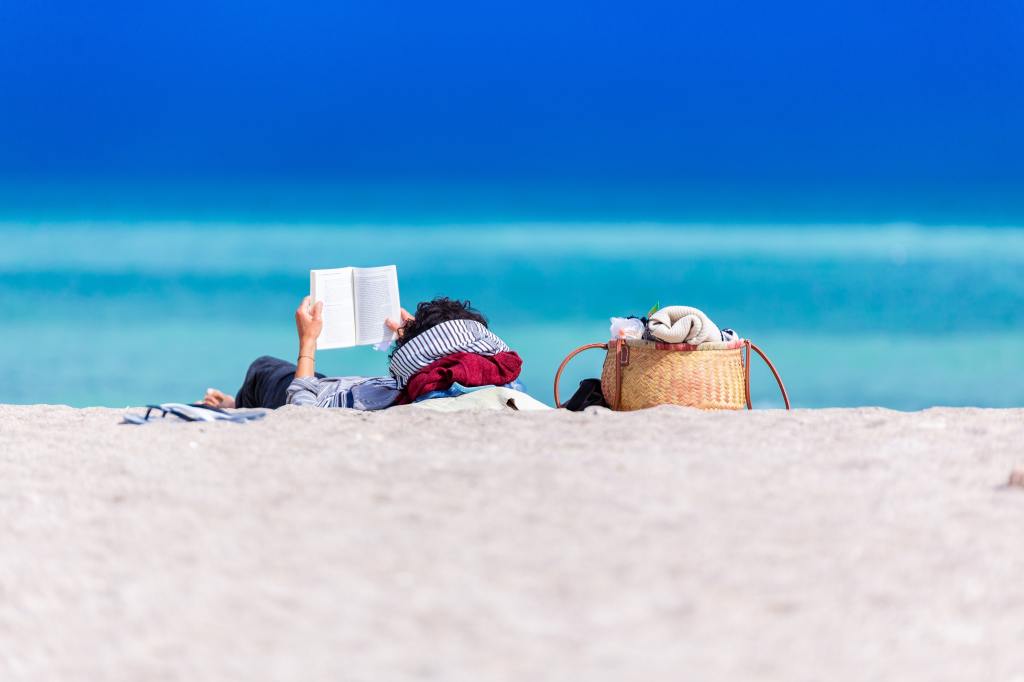 person reading a book while laying on the beach
